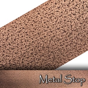Puede incluir: Primer plano de una superficie de metal cobre texturizada. La superficie tiene un aspecto rugoso y martillado. El texto "Metal Stop" está impreso en blanco en la parte inferior de la imagen.