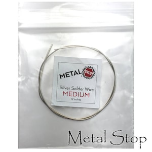 Könnte beinhalten: Eine transparente Plastiktüte mit einer Spule aus Silberlotdraht. Ein weißes Etikett in der Tüte trägt die Aufschrift "METAL STOP" mit "Silver Solder Wire MEDIUM 30.48 cm". Der Markenname "Metal Stop" ist unten aufgedruckt.