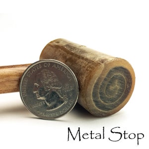 May include: A close-up of a wooden mallet with a metal stop. The mallet is about the size of a US quarter.