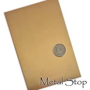 Pode incluir: Uma chapa retangular de metal cor de cobre com uma moeda na superfície. O texto "Metal Stop" está impresso em preto na parte inferior. A chapa tem uma superfície lisa e reflexiva. A moeda tem cerca de 2,4 cm de diâmetro.