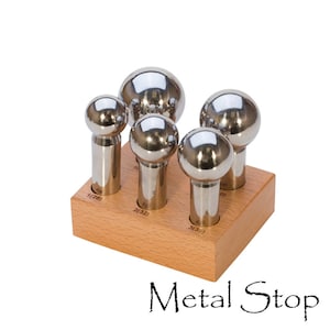 Puede incluir: Conjunto de cinco punzones de bola de metal plateado en un soporte de madera. El soporte tiene etiquetas para cada tamaño de punzón: 1/28, 2/32, 3/32, 4/32 y 5/32.