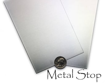 Könnte beinhalten: Zwei gebürstete Metallplatten, wahrscheinlich Stahl oder Aluminium, sind gegeneinander geneigt. Eine Münze befindet sich unten als Größenreferenz. Der Text "Metal Stop" ist in einer Schreibschrift geschrieben.
