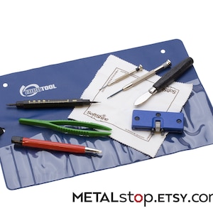 Könnte beinhalten: Eine blaue Uhrenreparaturmatte mit verschiedenen Werkzeugen, darunter ein Uhrengehäuseöffner, eine Pinzette, ein Schraubendreher, ein Messer und ein Poliertuch. Die Matte trägt den Schriftzug "EUROTOOL".