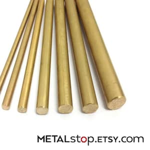 Puede incluir: Colección de varillas de latón de varios diámetros, dispuestas sobre un fondo blanco. Las varillas tienen un tono dorado y son cilíndricas. El texto "METALstop.ETSY.com" es visible en la parte inferior.