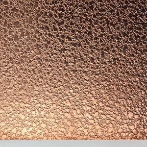 May include: A copper-colored metal sheet with a textured surface, next to a quarter. The sheet has a bubbly, irregular pattern. The text "Metal Stop" is at the bottom of the image.