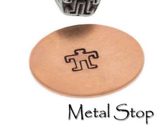 May include: A metal stamp with a human figure design, alongside a stamped copper disc. The stamp is made of a dark, textured metal. The copper disc has a circular shape with the stamped figure in the center. The text "Metal Stop" is at the bottom.