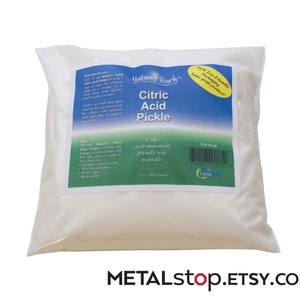 以下が含まれることがあります： 自然のタッチ クエン酸ピクルスの白い袋。安全で環境に優しいピクルスの方法です。袋には使用方法とバーコードが記載されています。袋は白い表面の上にあります。