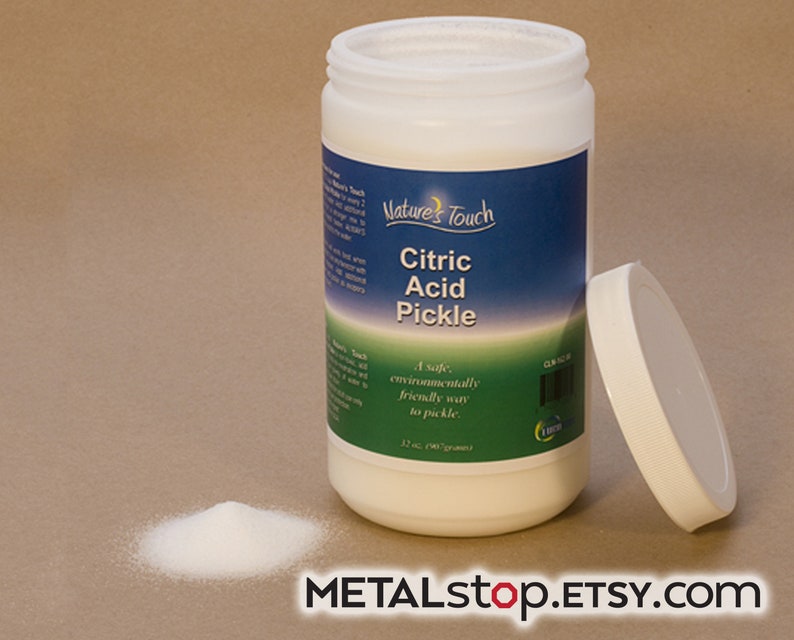 May include: A white plastic container of citric acid pickle, with a white lid off to the side. The container has a blue label with the text "Nature's Touch Citric Acid Pickle" and a green label with the text "A safe, environmentally friendly way to pickle". There is a small pile of white powder in front of the container.