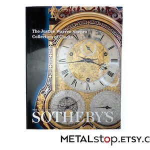 May include: A book cover titled The Justice Warren Shepro Collection of Clocks featuring a detailed photograph of an ornate gold and silver clock face with Roman numerals and multiple sub-dials, with the Sotheby's logo printed at the bottom.