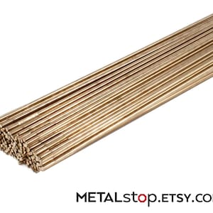 Pode incluir: Um feixe de finas varetas met&aacute;licas douradas, provavelmente lat&atilde;o ou uma liga semelhante, dispostas em uma pilha organizada. As varetas s&atilde;o paralelas e uniformemente espa&ccedil;adas, refletindo a luz. O nome da loja Etsy, METALstop.ETSY.com, &eacute; vis&iacute;vel na parte inferior.