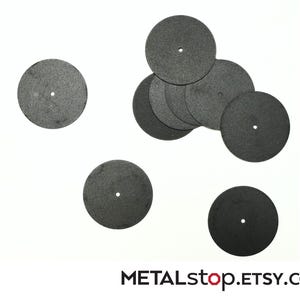 Può includere: Una collezione di dischi da taglio circolari grigio scuro con un piccolo foro centrale, sparsi su uno sfondo bianco. I dischi sembrano essere fatti di un materiale strutturato. Il nome del negozio Etsy "METALstop.ETSY.com" è visibile in basso.
