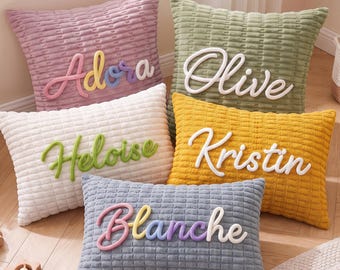 May include: Five rectangular and square throw pillows with a textured grid pattern. The pillows are mauve, sage green, white, mustard yellow, and slate blue. Each pillow features a raised, cursive name: Adora, Olive, Heloise, Kristin, and Blanche.