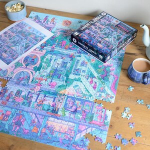 May include: A partially assembled jigsaw puzzle with a colorful cityscape design, titled "Concrete Jungle." The puzzle is on a wooden surface, with the box and a print of the image visible. A cup of tea and popcorn are also present.