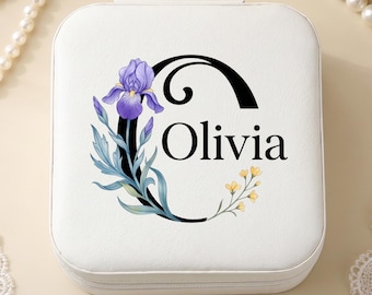 May include: A square white jewelry box featuring a large black letter C printed on the top. The letter is decorated with a purple iris flower and green leaves on the left side and small yellow flowers on the right. The name Olivia is printed in black.