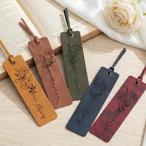 May include: Five leather bookmarks in various colors, each with a floral design and a name. The bookmarks are tan, brown, green, blue, and burgundy. Each bookmark has a leather strap attached at the top. A book and a white rose are in the background.