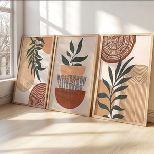 Pode incluir: Três impressões de arte emolduradas com designs botânicos abstratos. Cada impressão apresenta uma paleta de cores neutras com detalhes em terracota, bege e verde escuro. A obra de arte inclui ilustrações de folhas e plantas, formas geométricas e padrões texturizados.