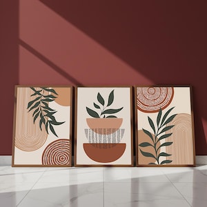Puede incluir: Tres impresiones artísticas enmarcadas con un tema botánico minimalista. Cada impresión presenta un fondo beige con formas abstractas en marrón, terracota y verde. Las impresiones incluyen diseños de hojas y plantas, y patrones geométricos.