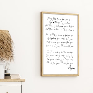 Può includere: Una stampa incorniciata con una cornice in legno chiaro. Lo sfondo bianco presenta un testo scritto a mano nero di una preghiera. La preghiera include frasi come "Possa il suo favore essere su di te" e "Lui è con te."