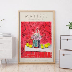 May include: A framed poster for a Matisse exhibit at the Museum of Modern Art. The poster features a still life painting of a vase with flowers and fruit against a red background. The text "MATISSE" is printed in black at the top of the poster.