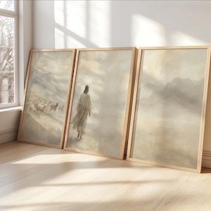 May include: Three framed art prints with a religious theme. The prints feature a muted color palette of beige, gray, and white. One print depicts a figure walking, another shows a flock of sheep, and the third shows a mountain range.