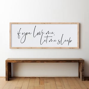 Op de afbeelding: Een ingelijst houten bord met de tekst "if you love me, let me sleep" geschreven in zwarte cursieve letters.