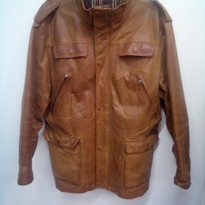May include: A brown leather jacket with a zipper closure and multiple pockets. The jacket has a stand-up collar and a lined interior.