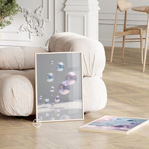 Peut inclure: Deux impressions d'art encadrées avec des cadres en bois clair. L'une représente des bulles irisées flottantes sur fond gris. La seconde présente un schéma de couleurs pastel avec du texte. Les impressions sont exposées sur un parquet clair.