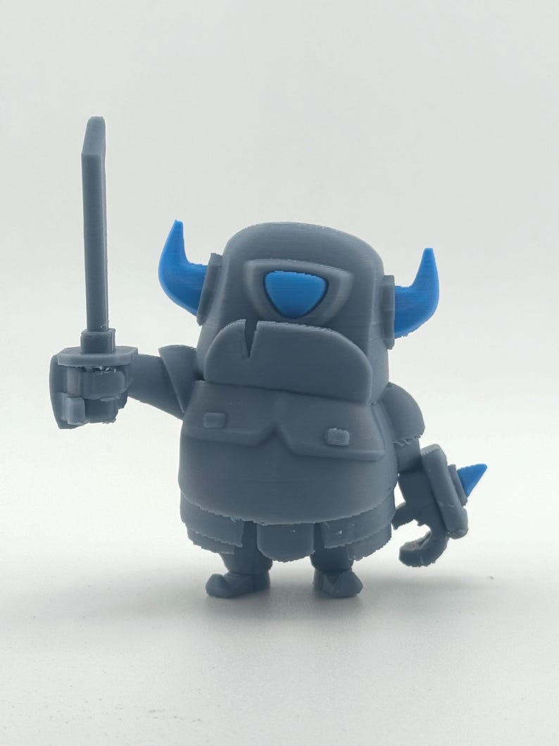 May include: A gray 3D printed figurine of a stout armored character with bright blue horns and a blue visor. The figure holds a gray sword in its right hand and features a rounded body, segmented armor plating, and small feet on a plain background.