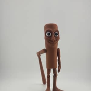 May include: A brown, articulated figurine with a cylindrical body, large eyes, and a smiling face. The figure is holding a brown bat and has articulated arms and legs. The figurine is standing on a white surface.