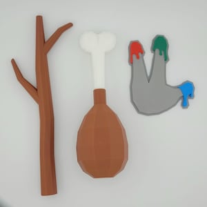 May include: A collection of three whimsical, cartoon-style objects: a brown tree, a drumstick, and a gray hand with colorful paint drips in red, green, and blue. The objects are rendered with a low-poly design.