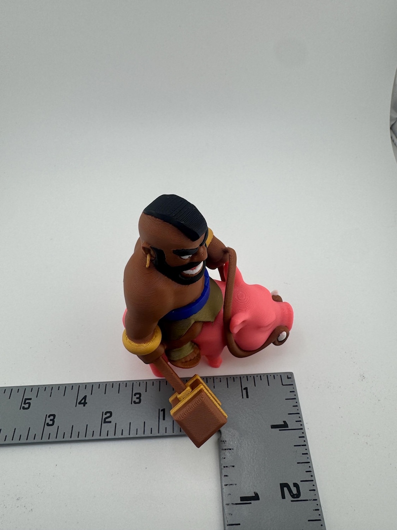 Puede incluir: Figura impresa en 3D de un personaje del juego Clash of Clans. El personaje es un hombre de piel oscura con una cresta negra, montado en un cerdo rosa. Sostiene un martillo marr&oacute;n. La figura mide aproximadamente 7.6 cm de altura.