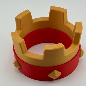 Puede incluir: Una corona impresa en 3D en dos partes. La base es roja y la parte superior es dorada. La corona tiene puntas rectangulares y detalles en forma de diamante. Este art&iacute;culo decorativo es adecuado para cosplay o eventos tem&aacute;ticos.
