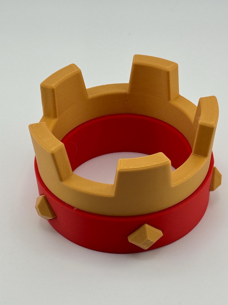 Puede incluir: Una corona impresa en 3D en dos partes. La base es roja y la parte superior es dorada. La corona tiene puntas rectangulares y detalles en forma de diamante. Este art&iacute;culo decorativo es adecuado para cosplay o eventos tem&aacute;ticos.