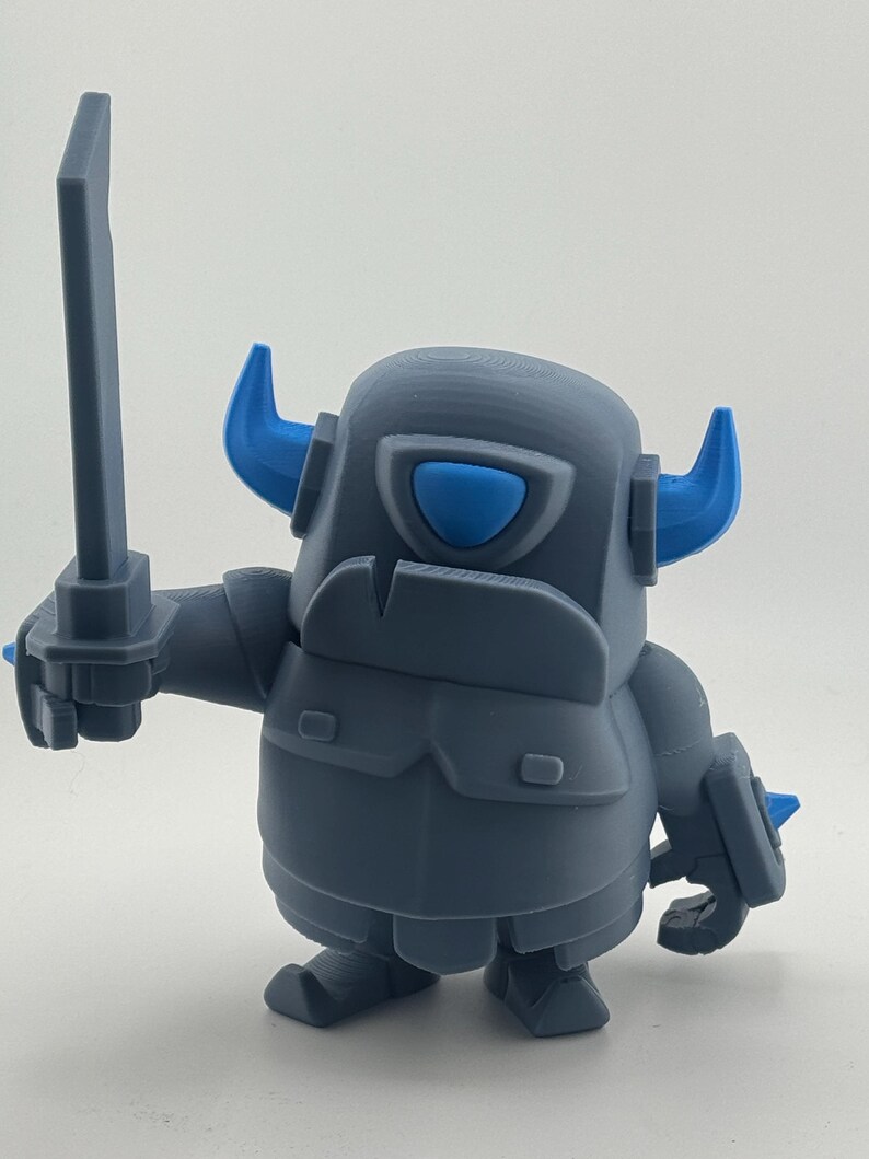 May include: A gray plastic figurine of a knight character with a rounded body, wearing armor with blue horns and a blue visor. The figure holds a gray sword in its right hand and has a small shield on its left arm, featuring a smooth, matte finish.
