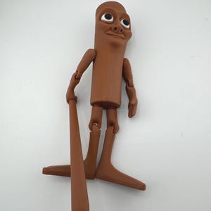 May include: A brown articulated figure with a cylindrical body, arms, and legs. The figure has a smiling face and is holding a brown baseball bat. The figure's limbs are jointed, allowing for posing. The figure is standing on a white surface.