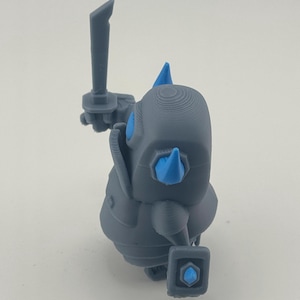 May include: A gray 3D printed figurine of a stylized warrior character. The figure features a rounded body, a sword held upright in one hand, and a small shield in the other. Bright blue accents are visible on the eyes, shoulder spikes, and shield.