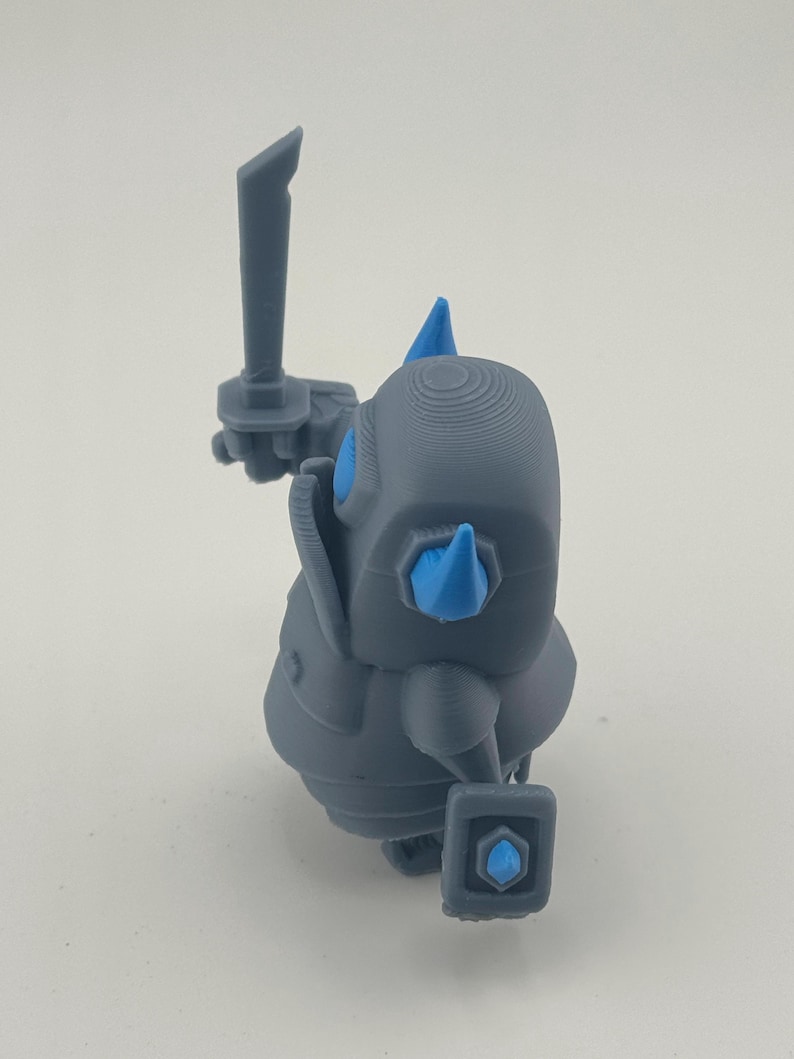 May include: A gray 3D printed figurine of a stylized warrior character. The figure features a rounded body, a sword held upright in one hand, and a small shield in the other. Bright blue accents are visible on the eyes, shoulder spikes, and shield.