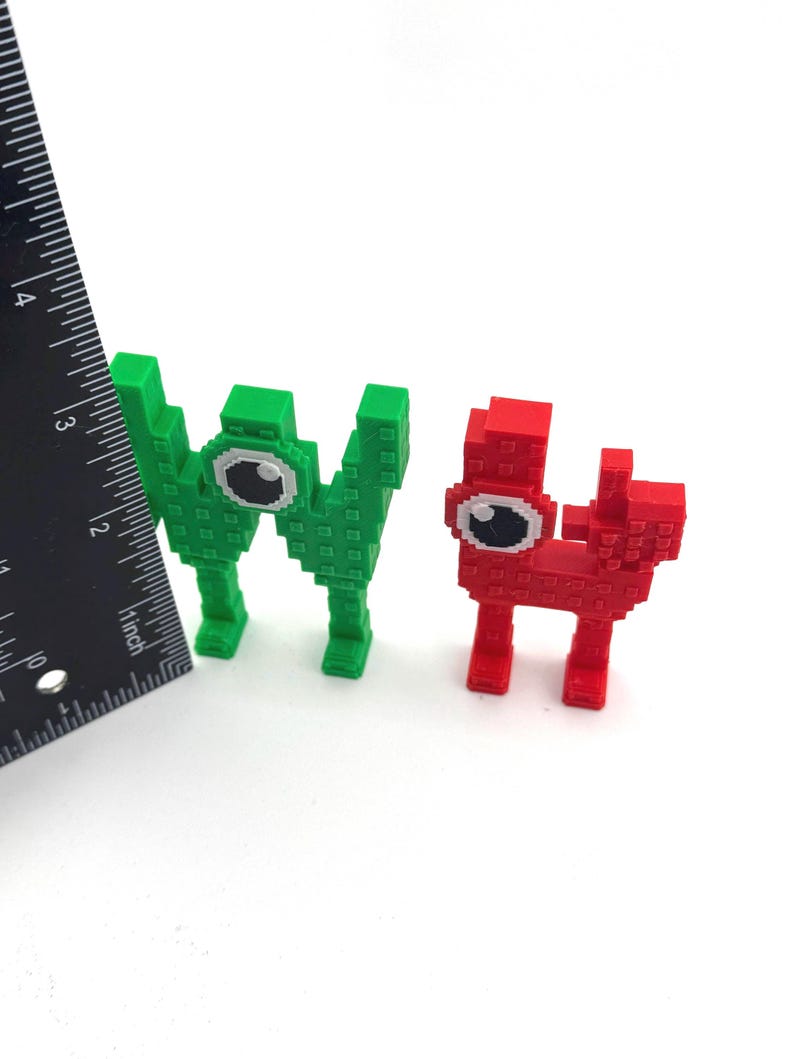 May include: Two pixelated figures, one green and one red, each with a large eye. The green figure is taller and resembles the letter "W". The red figure is shorter and has a more rectangular shape. A ruler is placed next to the figures.