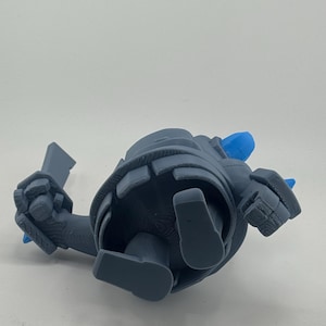 May include: A gray 3D printed figurine of a character with a rounded body, blocky limbs, and a sword in one hand. The figure features bright blue accents on the head and back, with visible layer lines from the printing process on the surface.