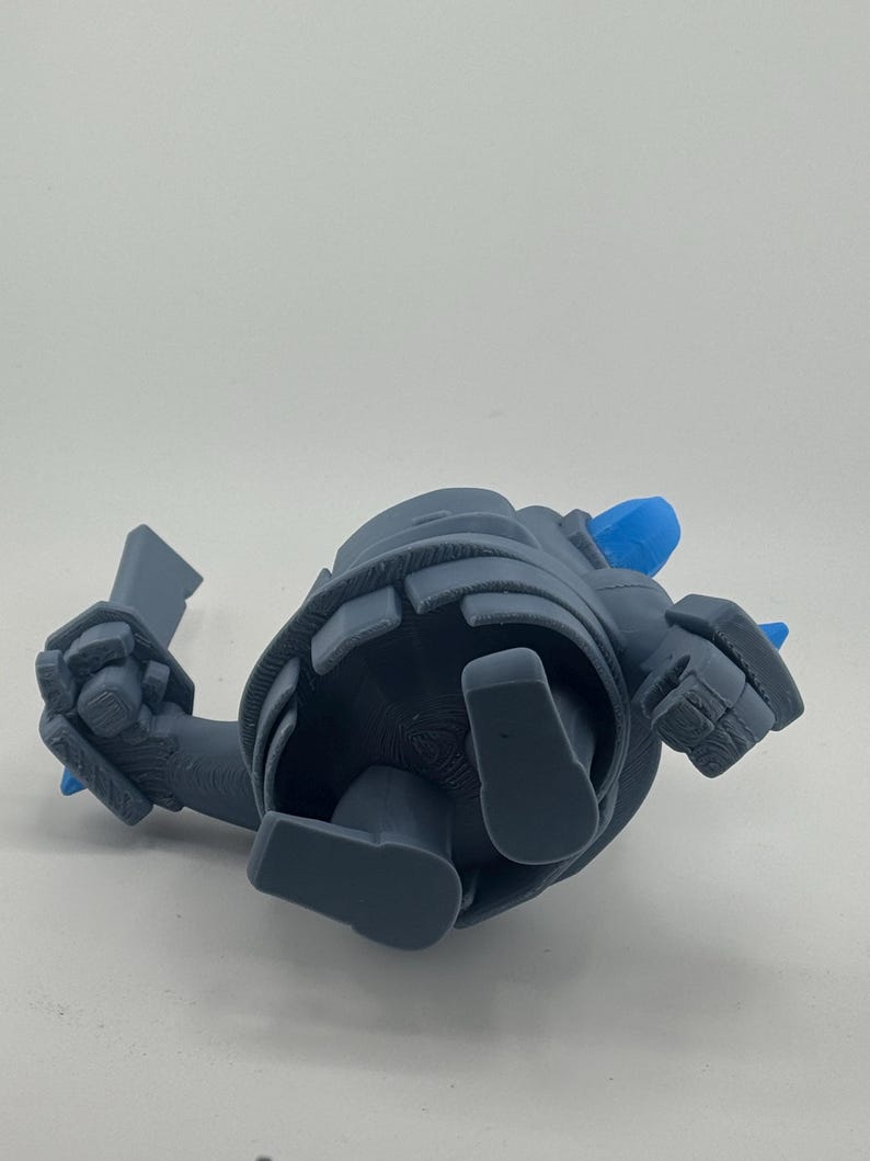 May include: A gray 3D printed figurine of a character with a rounded body, blocky limbs, and a sword in one hand. The figure features bright blue accents on the head and back, with visible layer lines from the printing process on the surface.