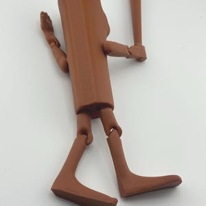 May include: A brown articulated figure holding a baseball bat. The figure has a rectangular torso, jointed limbs, and a rounded head. The baseball bat is also brown and is held in the figure's right hand.