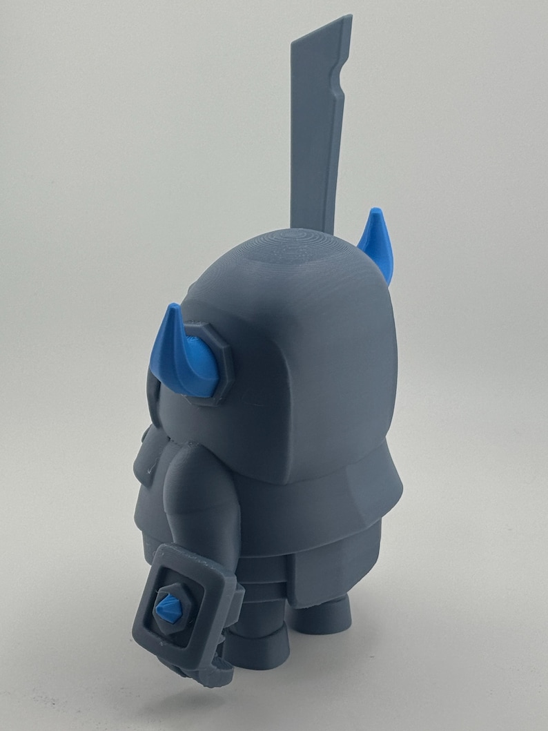 May include: A gray 3D printed figurine of a knight character with a large sword extending from the back. The figure features two bright blue horns on the helmet and a small blue accent on the shield held in the hand, with a smooth matte finish.