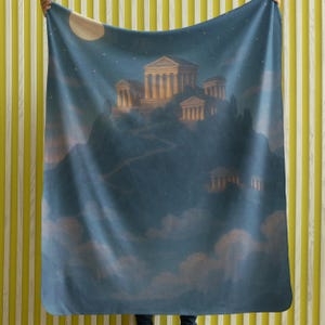 May include: A blue blanket featuring a nighttime landscape with a classical building on a hill, illuminated by a full moon and stars. The design includes clouds and a winding road leading to the structure. The blanket is held up against a yellow and white striped background.