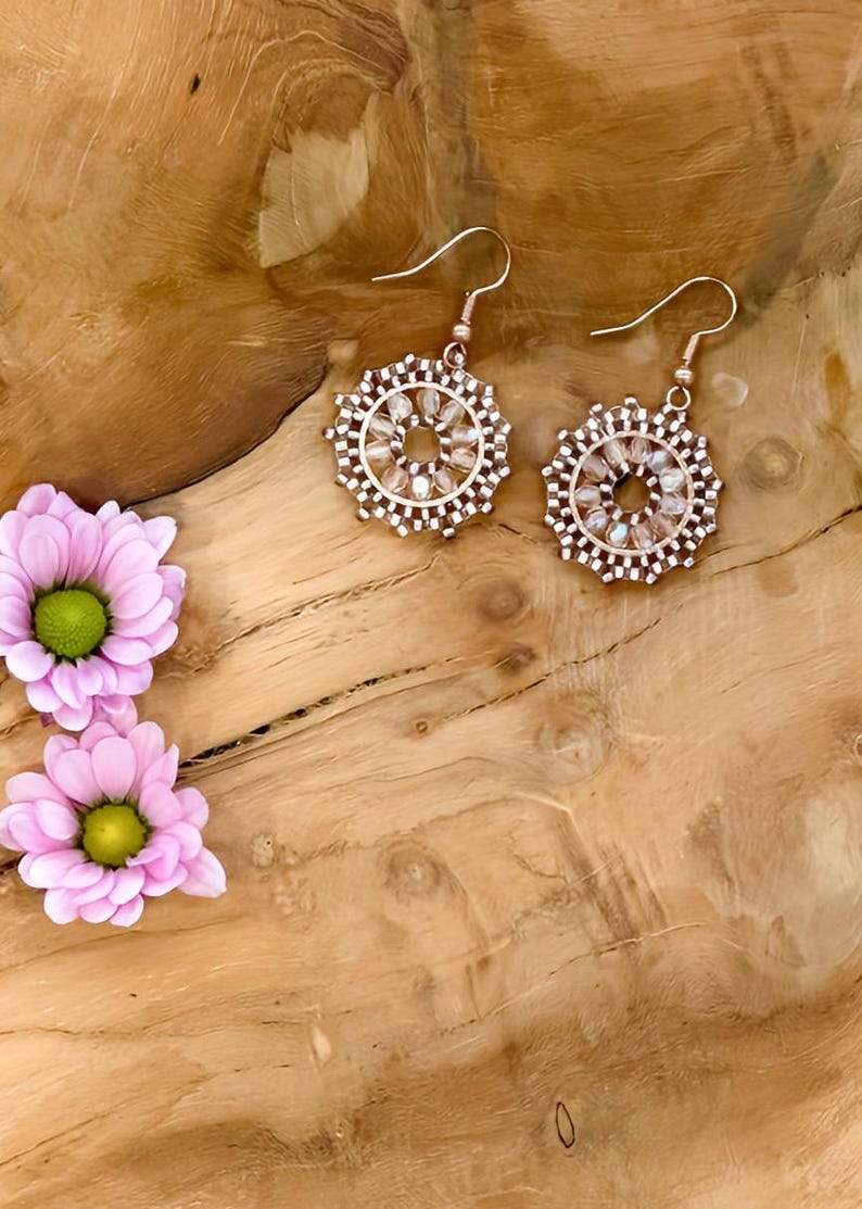 May include: A pair of dangle earrings with a circular design. The earrings are made of small, clear beads and have a rose gold finish.