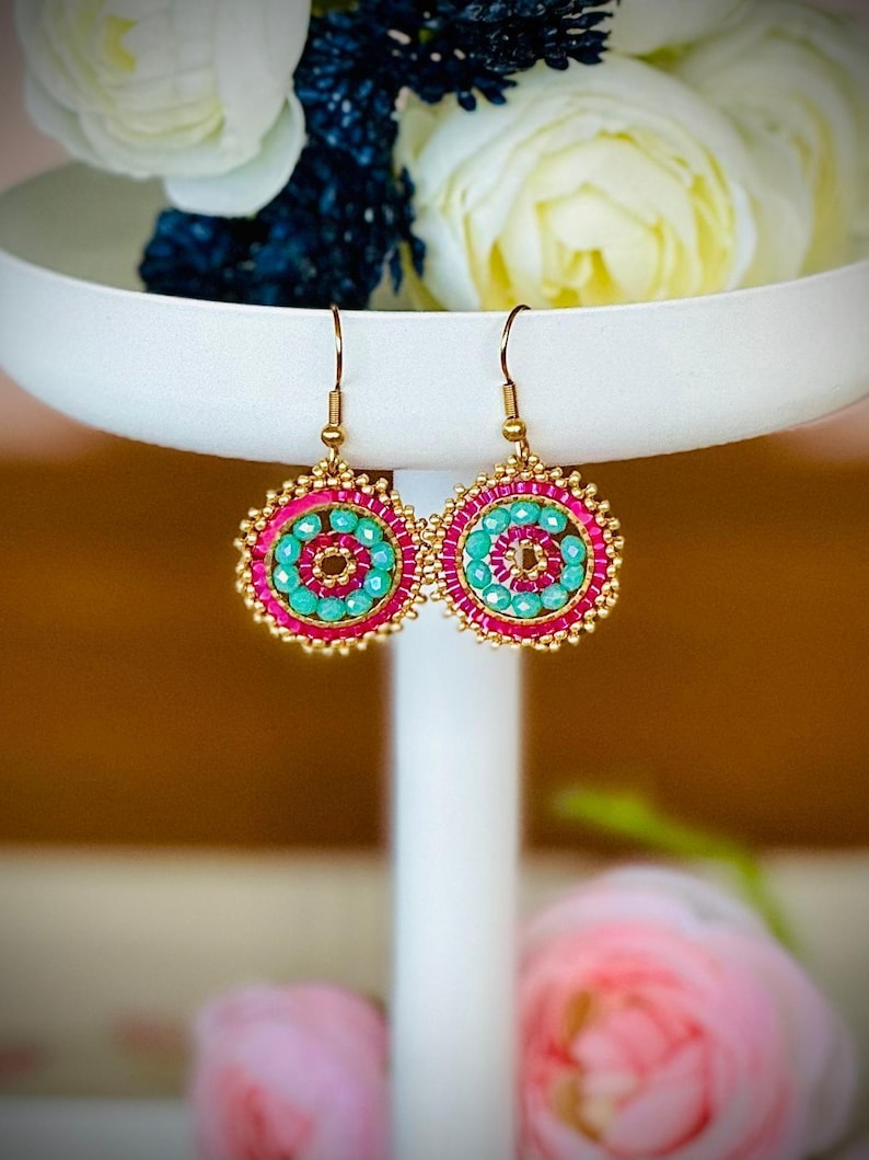 May include: A pair of gold hoop earrings with pink and turquoise beads. The earrings are on a white stand.