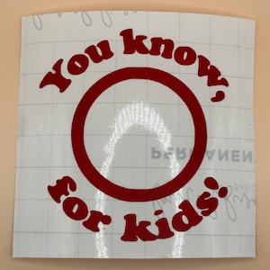 May include: A white sticker with the phrase "You know, for kids" in red, stylized lettering. The words surround a large red circle. The sticker is on a light beige background.