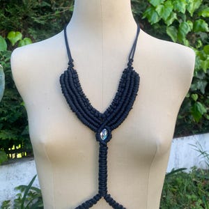 Peut inclure: Une chaîne de corps en macramé noire avec un grand pendentif en cristal transparent.