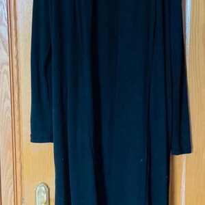 May include: A long, black cardigan hangs on a hanger. The open-front design features long sleeves and a knee-length hem. The cardigan is made of a soft, flowing fabric, perfect for layering.
