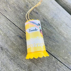 May include: Yellow pomander ornament with a white and yellow design featuring a rainbow and children. The ornament has a scalloped edge and a gold string.