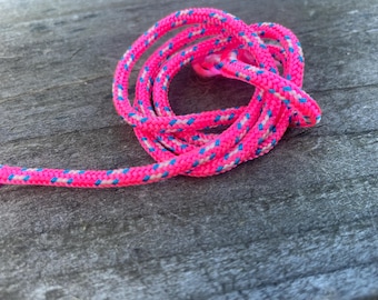 May include: A coiled, bright pink rope with a blue and white pattern. The rope is lying on a weathered, gray wooden surface. The rope is likely used for sports or crafts.